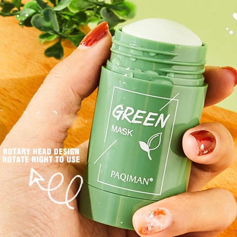 Green face mask stick held by a hand with a wooden surface and plant in the background