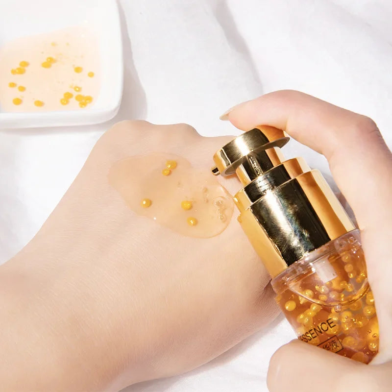 Gold serum bottle with a hand holding it, showing product on skin.